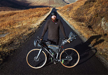 man standing by his bicycle on long road